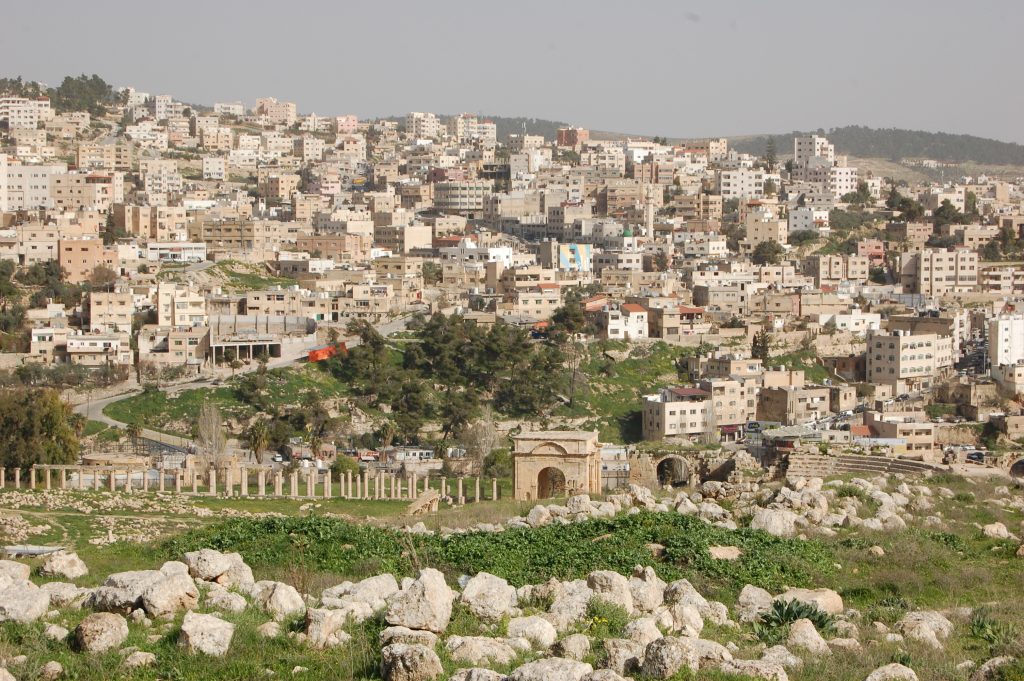Photo of parts of historic Jerash with modern buildings in the background.