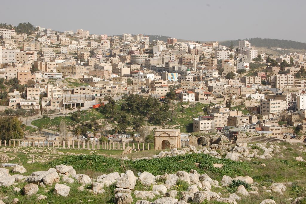 Foto af dele af det historiske Jerash med bygninger fra det moderne i baggrunden.