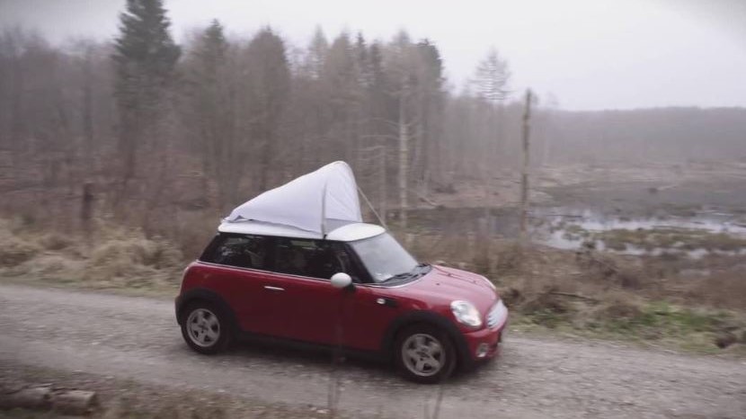 The photo shows a red car out in nature during the collection of insect with the insect net monitored on top of the car.