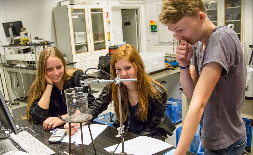 The image shows three high school students doing a scientific experiment. 