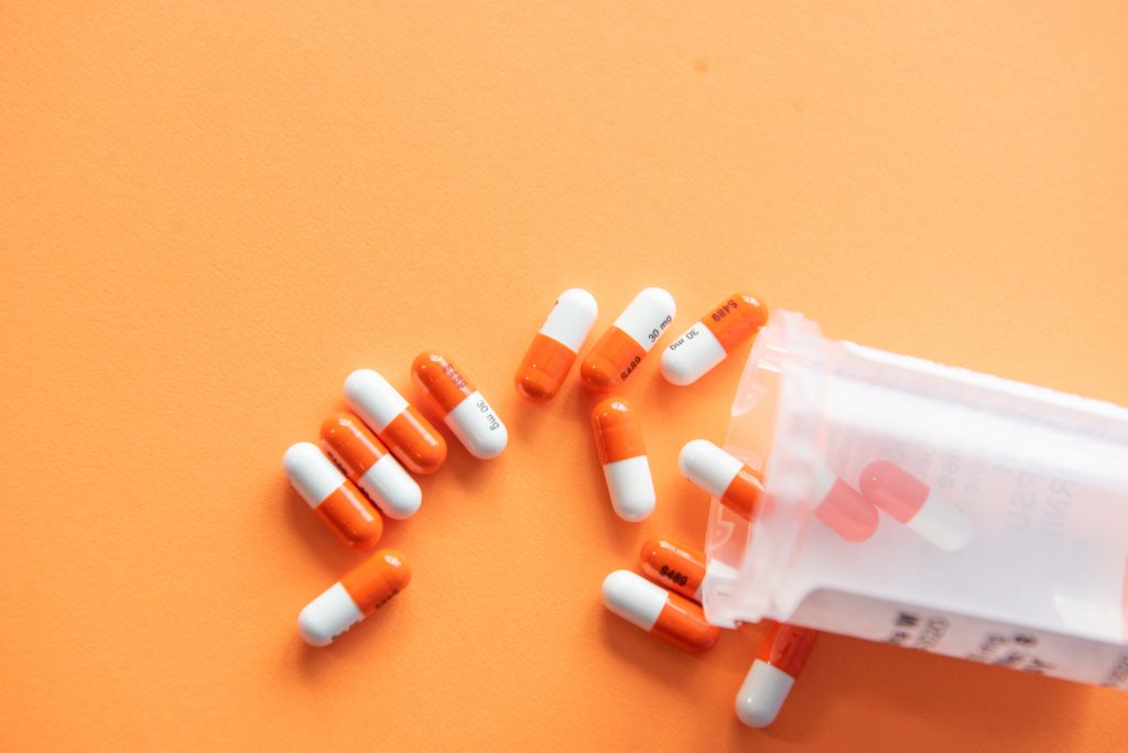 Billedet viser en håndfuld piller, som er væltet ud af et plastikpilleglas på en orange baggrund.