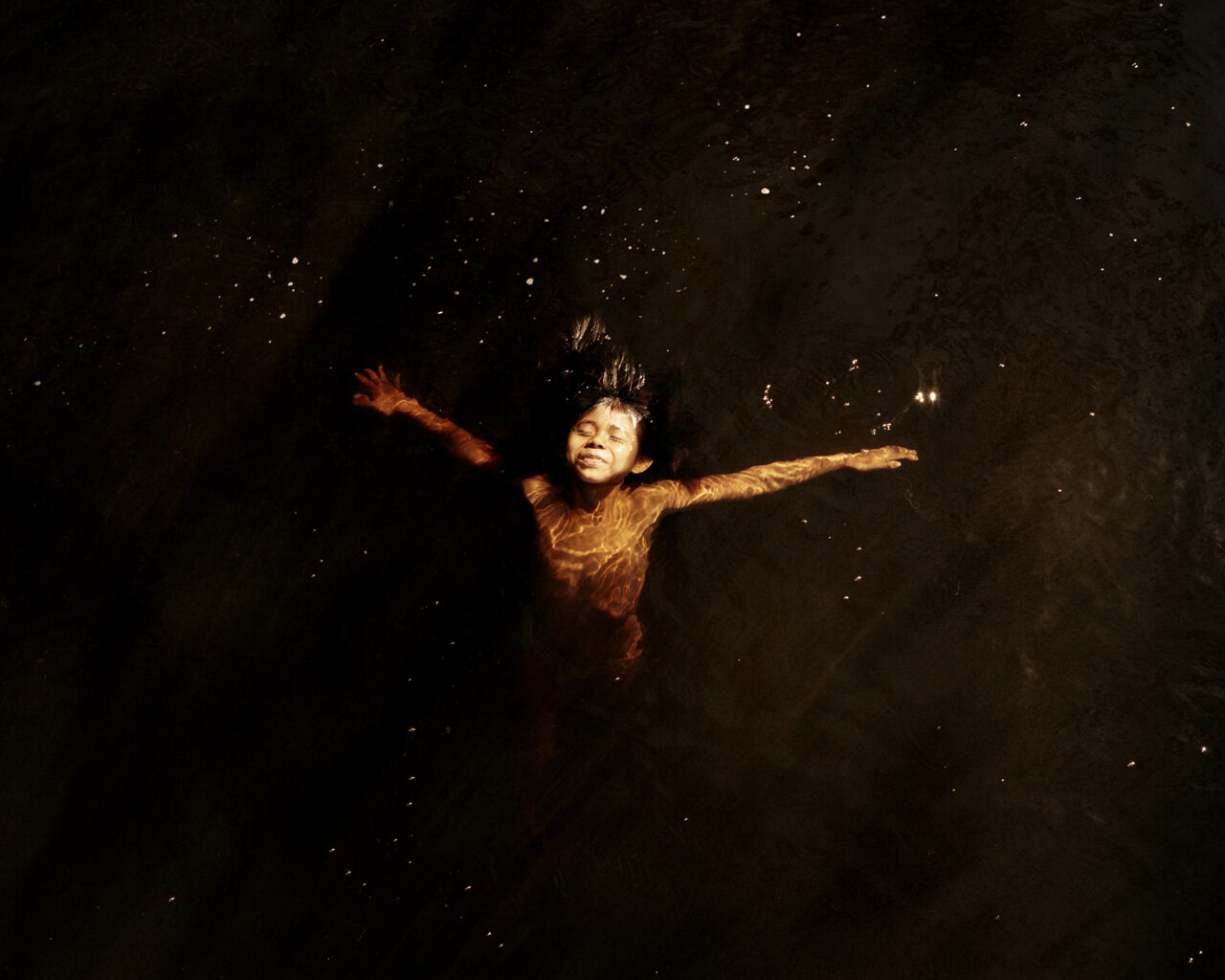 Girl floats in dark water with outstretched arms.